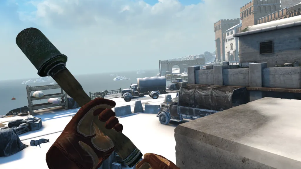 You are holding a grenade, ready to pull the pin. An enemy lies dead on the floor nearby and two vehicles ahead are primed for an explosive. A frozen sea and stone battlement feature in the background.