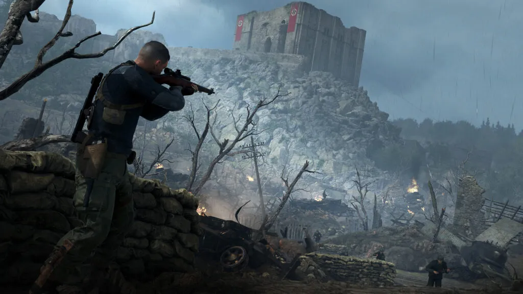 Karl Fairburne stands holding his Lee No.4 rifle. In the background a castle stands on top of rock rubble. Nazi flags align the battlements.
